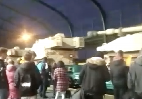 Screenshot from a Telegram video showing US M109 Paladin artillery systems on a westward train passing through a train station platform in Legnica, Poland. Text that accompanied the video inaccurately claimed the train was heading east.
