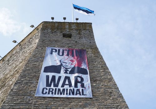 A banner reading “Putin War Criminal” hangs from the wall of Estonia’s Narva Fortress in the direction of Russia, as the neighboring Russian city of Ivangorod hosts a Victory Day concert in the direction of Narva, May 9, 2023. (Source: Reuters/Janis Laizans)