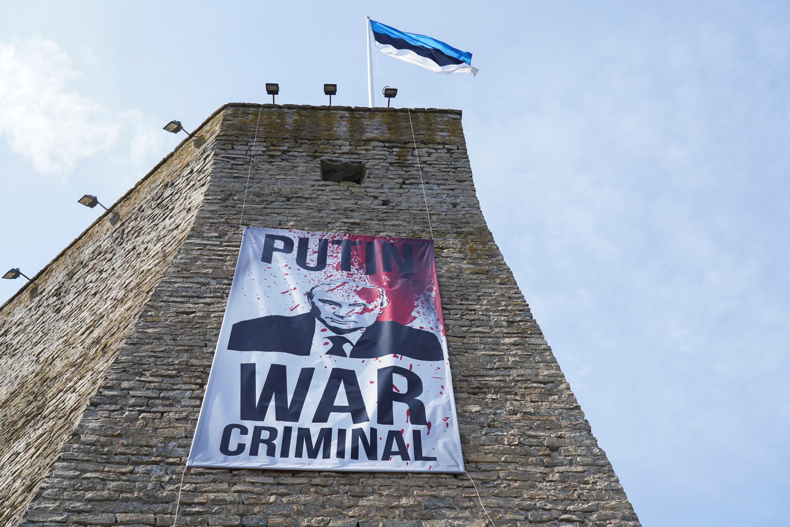 A banner reading “Putin War Criminal” hangs from the wall of Estonia’s Narva Fortress in the direction of Russia, as the neighboring Russian city of Ivangorod hosts a Victory Day concert in the direction of Narva, May 9, 2023. (Source: Reuters/Janis Laizans)